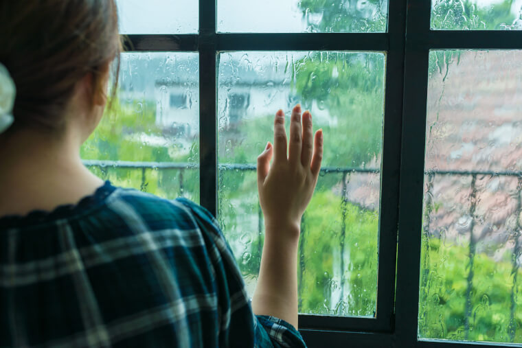 窓の外で雨が降る様子を見る女性