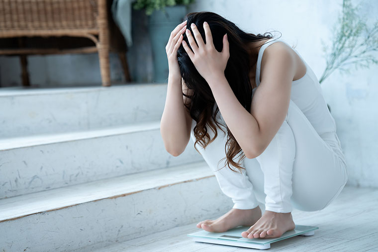 体重計にのって悩む女性