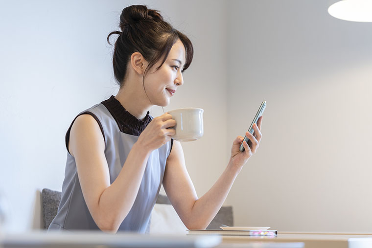 飲み物を飲みながらスマホを見る女性
