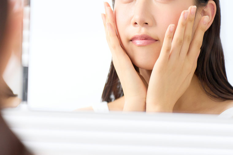 鏡を見ながら頬を触る女性