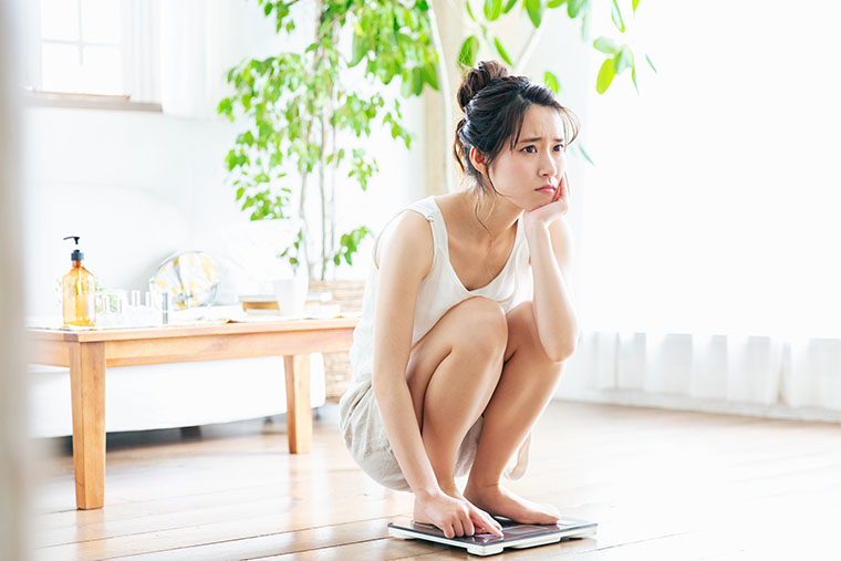 体重計の上で悩む女性